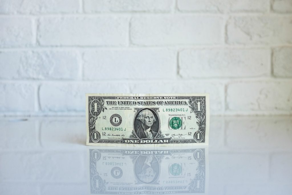 One dollar bill in front of white brick wall