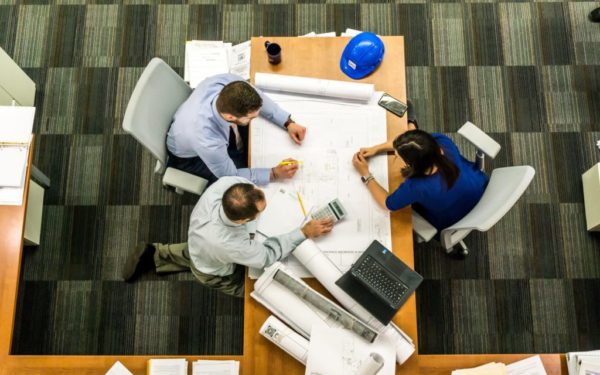 Birdseye view of 3 employees sitting around a desk looking at building plans