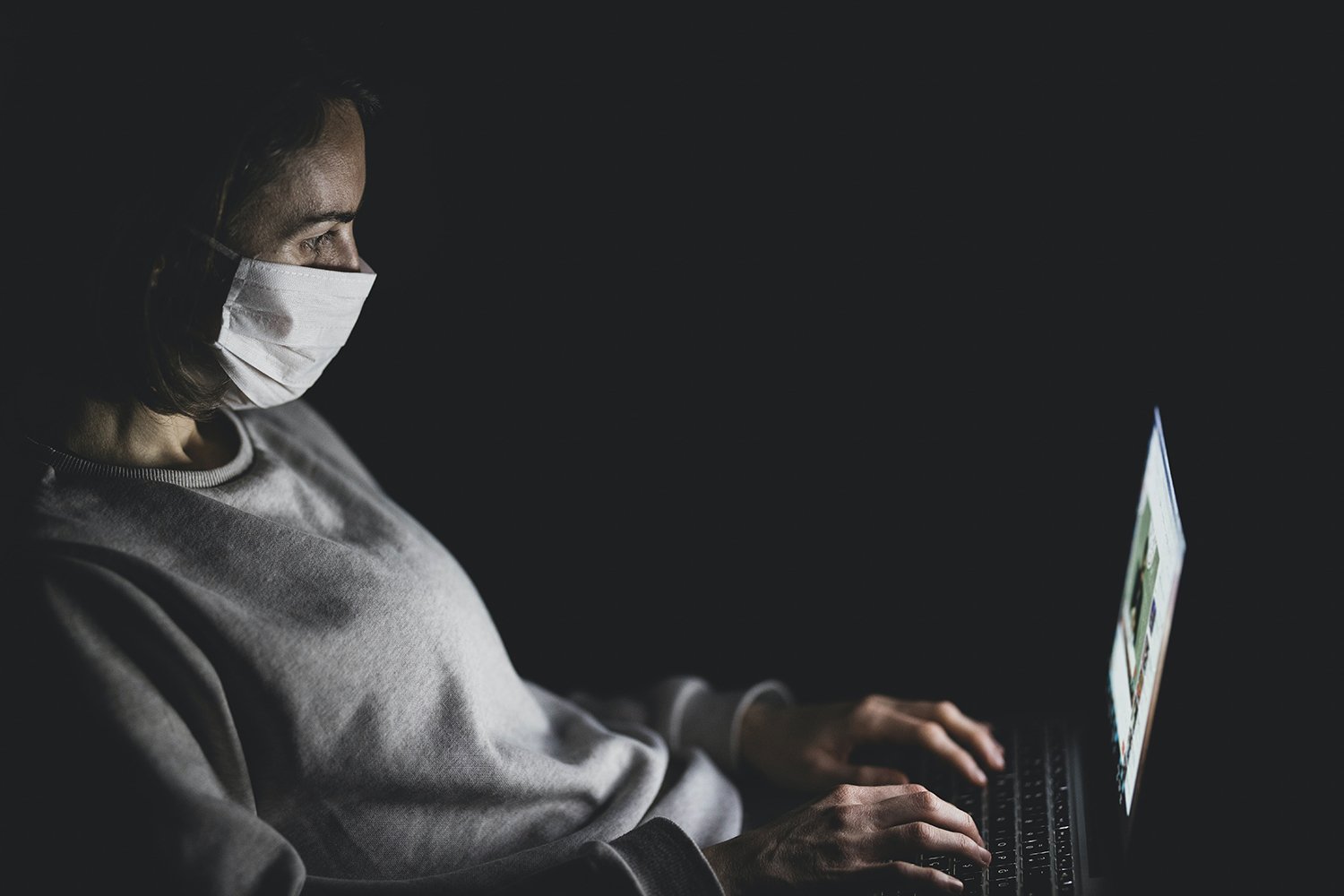 person wearing a face mask looking at their laptop