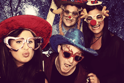 4 people taking photos in a photobooth wearing funny hats and glasses 