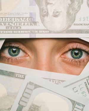 Eyeballs peaking through 100 dollar bills